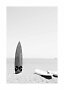 Schwarzweißfoto eines Surfbretts am Strand am Meer, daneben ein aufblasbares Board im Sand