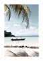 Small boat in shallow clear water by a sandy beach with palm leaves and calm sky