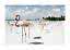 Flamingos standing in shallow water on a white sandy beach under a blue sky with clouds.