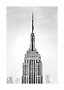 Sort-hvidt foto af Empire State Buildings top og spir mod en diset himmel.