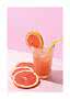 Glas mit rosa Grapefruitgetränk, Eis und gelbem Strohhalm neben Grapefruitscheiben auf rosa Hintergrund