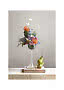 Blomsterarrangemang i hög glasvas med färgglada blommor och två päron på träblock