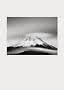 Black-and-white photo of a snow-covered mountain peak with soft clouds around it.