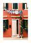 Coral house facade with green shutters, laundry hanging above, and flowers by the door